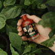 Hand holding a bottle of hot sauce amidst green leaves