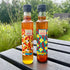 Two bottles of South End Chilli Farm oil and honey on a wooden surface with a garden background.