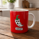 Red mug with ghost and chili pepper design on a wooden table in a kitchen.