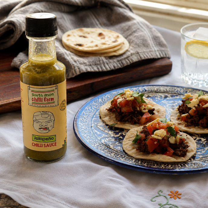 Bottle of Spicy Farm chili sauce with a plate of tacos on a table.